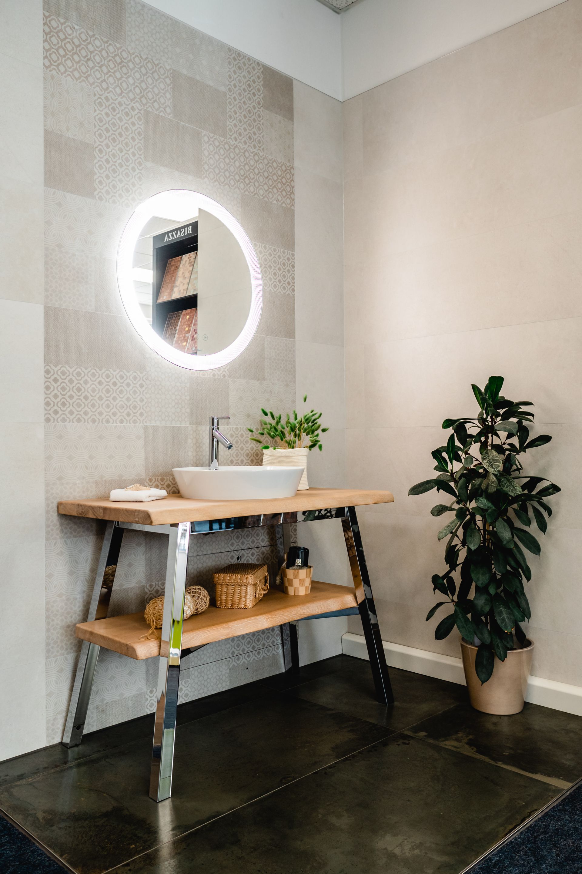 Badezimmer mit Holzwaschtisch, rundem Spiegel mit Beleuchtung und Topfpflanze.