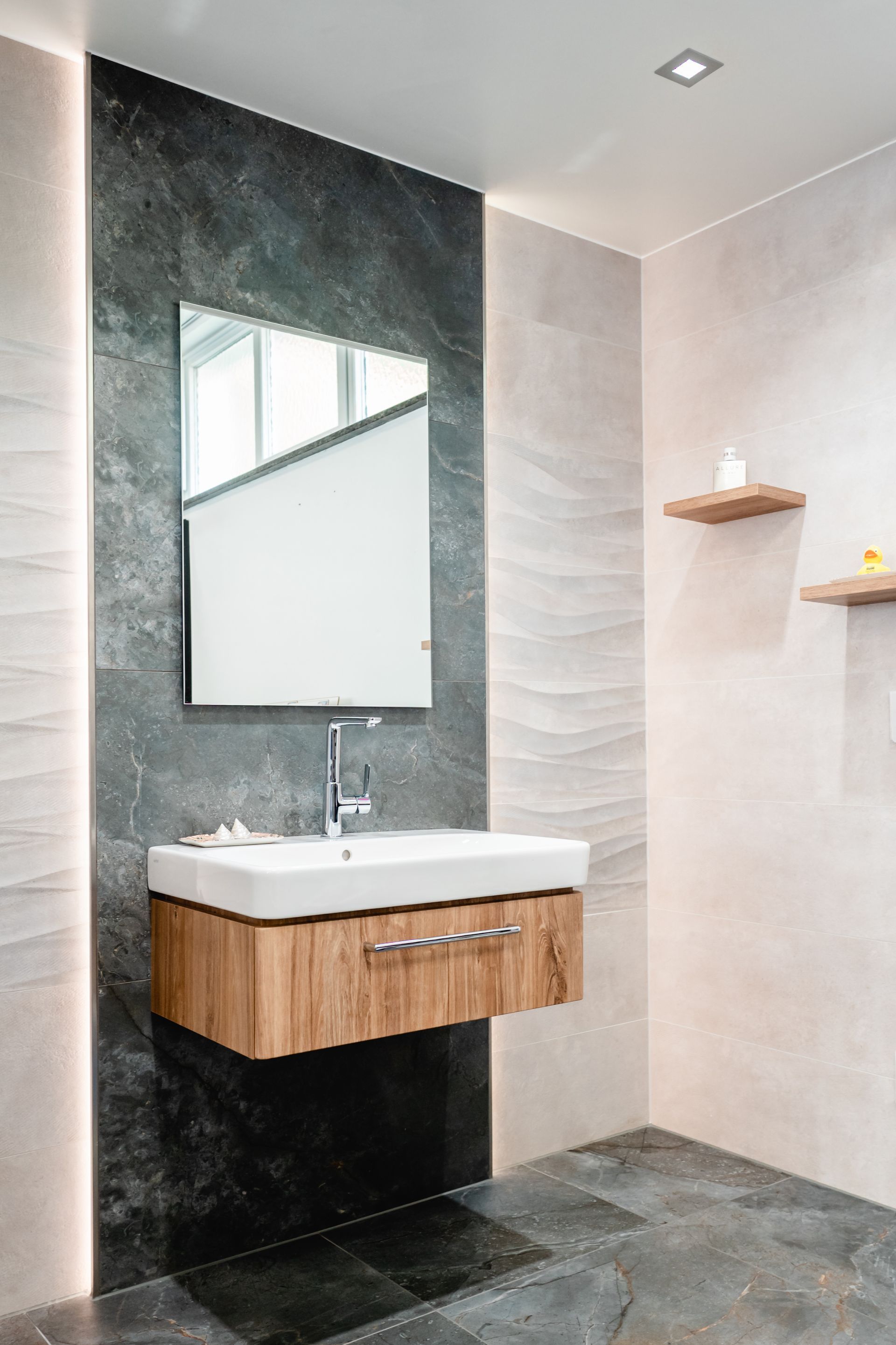 Modernes Badezimmer mit schwebendem Waschtisch aus Holz, Spiegel und grau/neutral gefliesten Wänden.