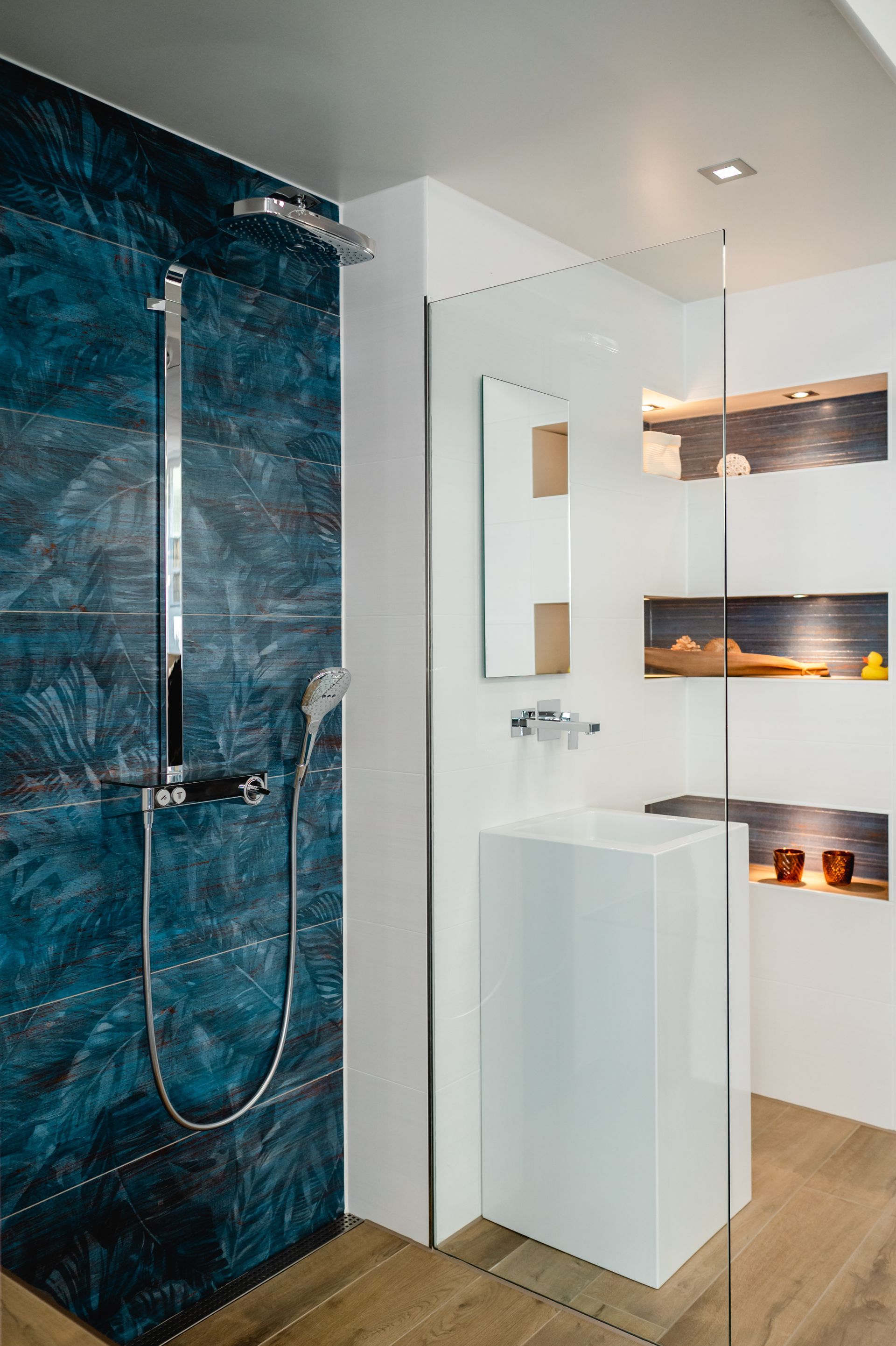 Modernes Badezimmer mit blau gefliester Dusche, weißem Waschbecken und eingebauten Regalen.