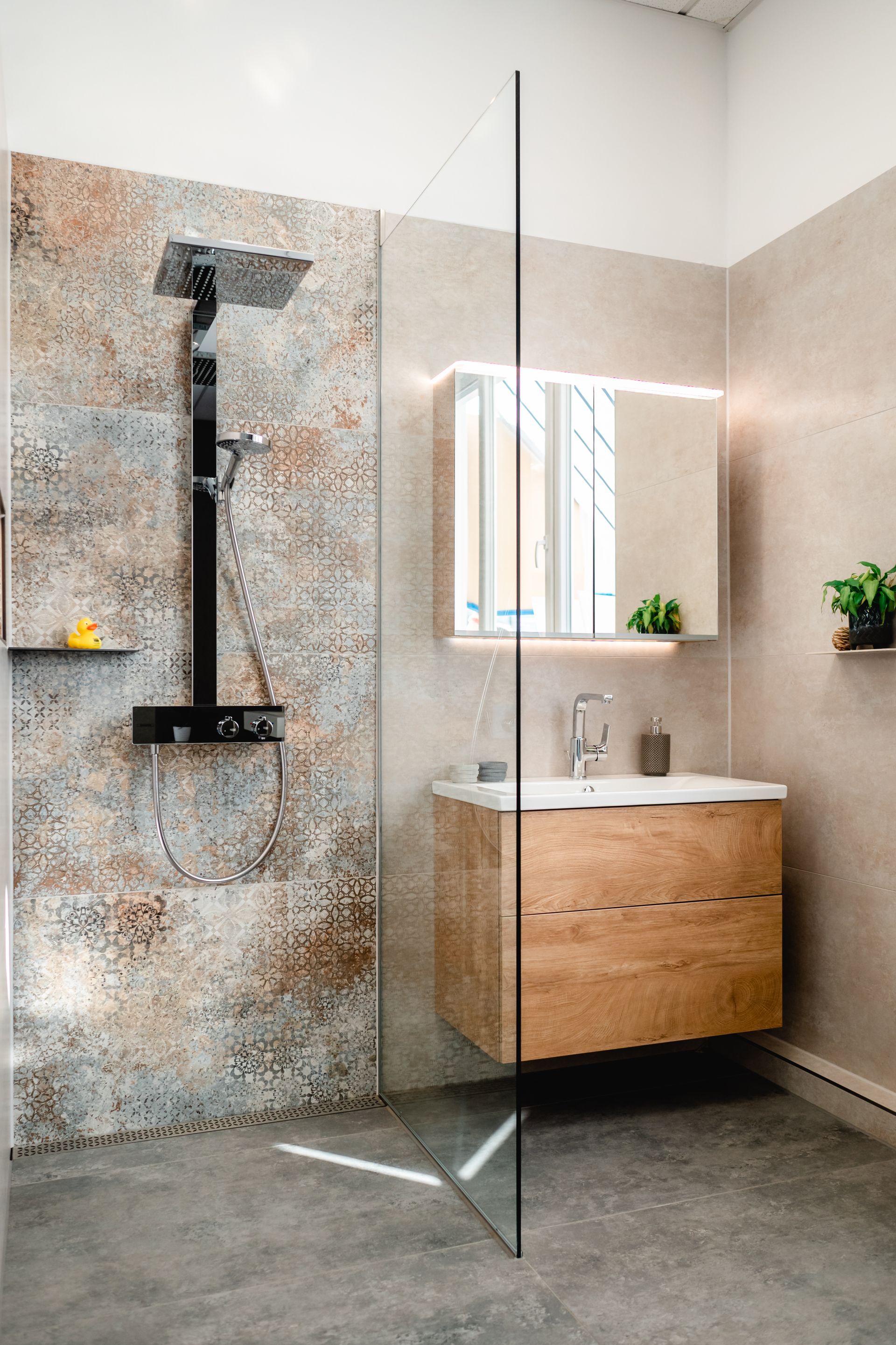 Modernes Badezimmer mit Dusche, Waschtisch und großem Spiegel. Braune und beige Fliesen, Holzschrank, Duschabtrennung aus Glas.