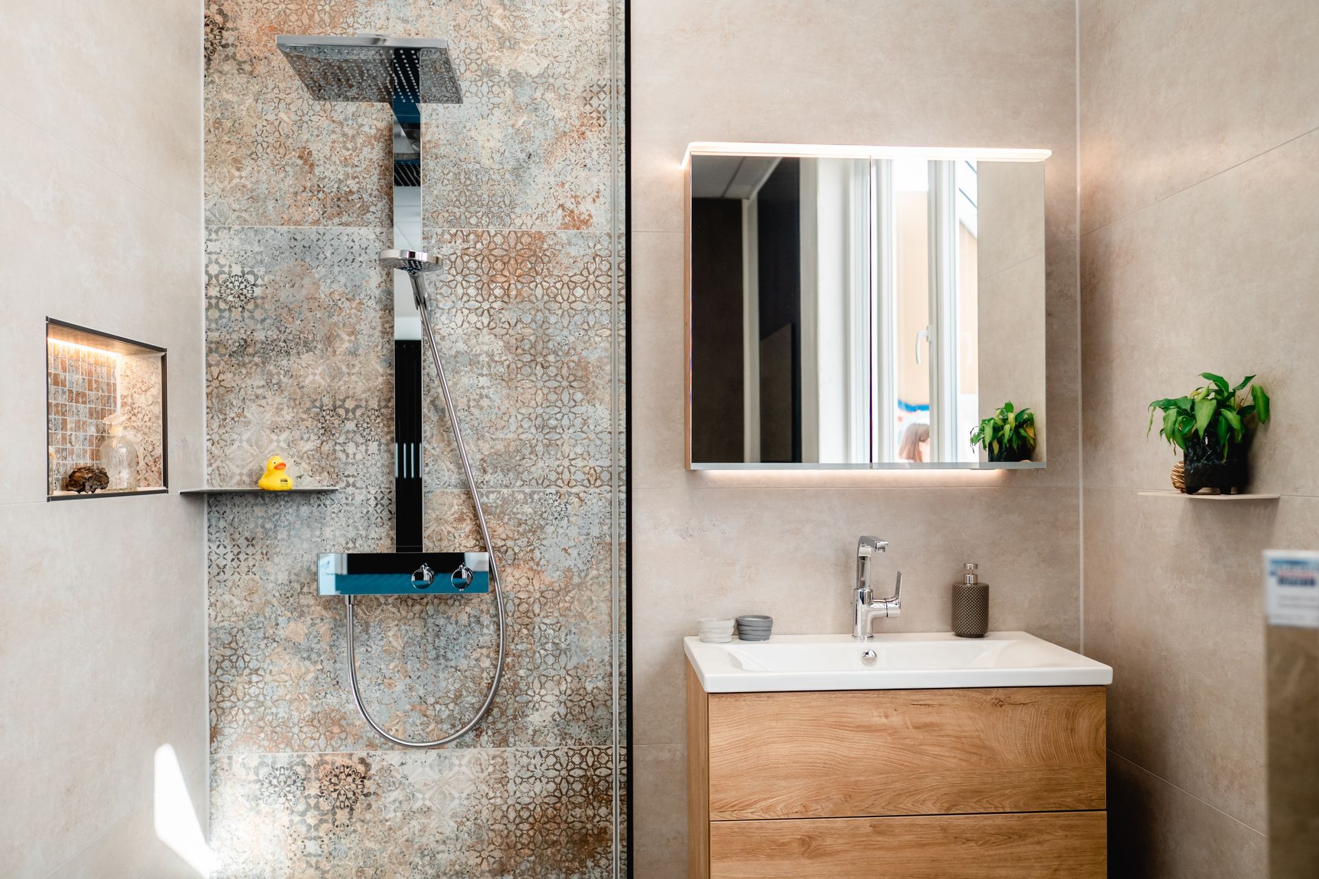 Modernes Badezimmer: Dusche mit gemusterten Fliesen, Holzwaschtisch und beleuchtetem Spiegel.