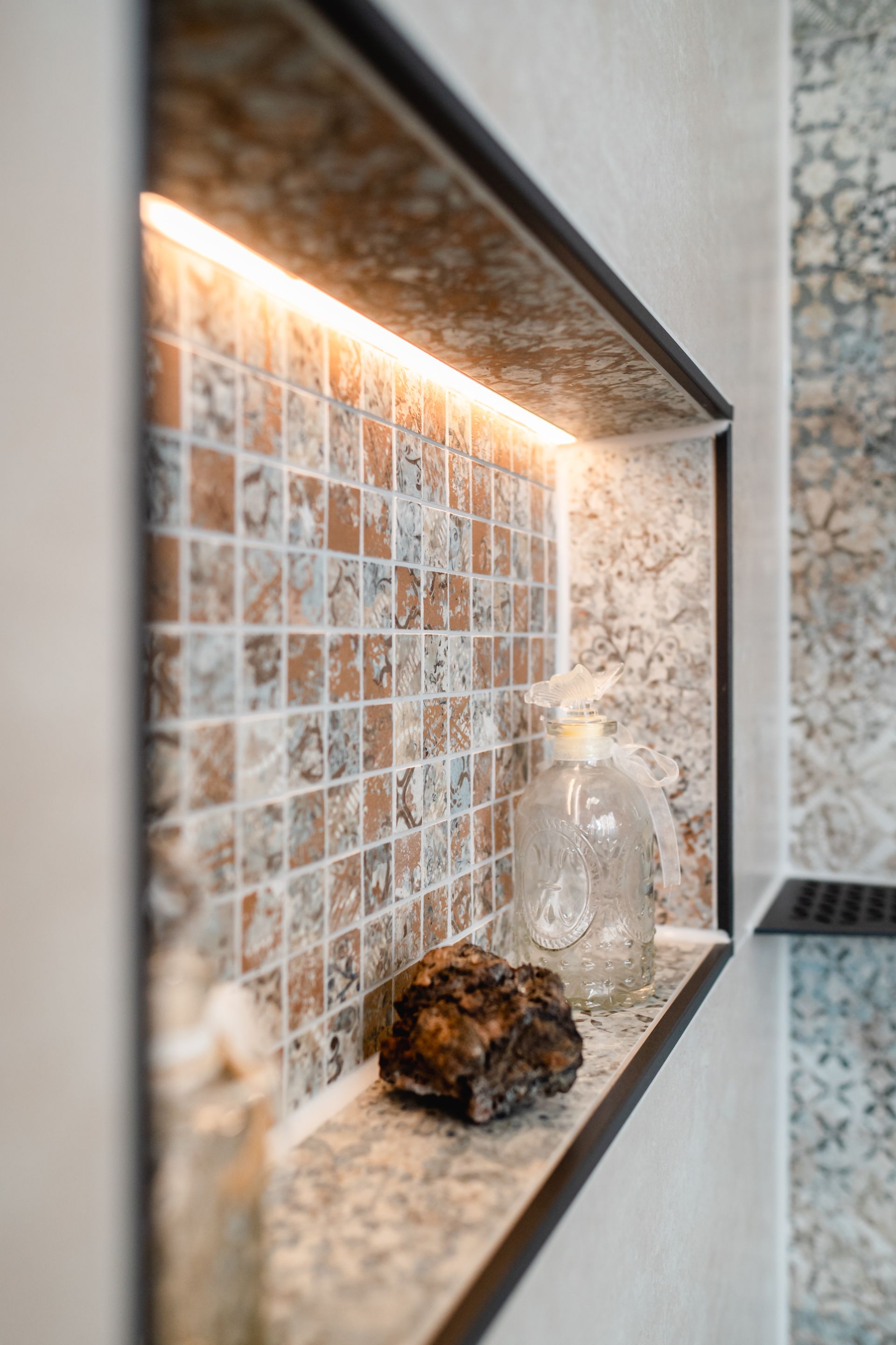 Eingelassenes Duschregal mit orangefarbenen und braunen Fliesen, beleuchtet durch einen LED-Streifen, mit einem Stein und Seife.