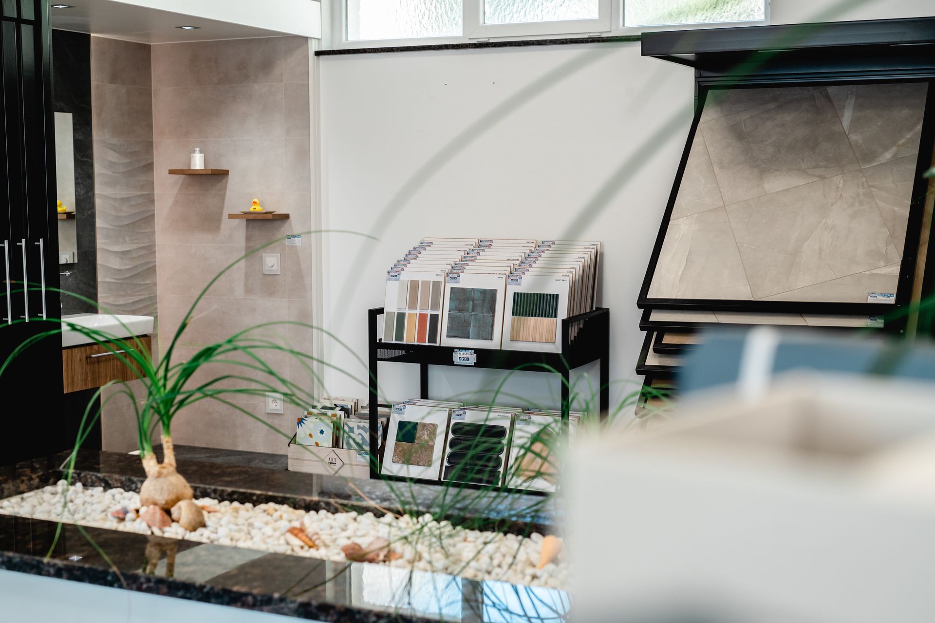 Ein Ausstellungsraum mit Fliesenmustern und Badezimmerarmaturen, mit dekorativen Pflanzen und in neutralen Farbtönen.