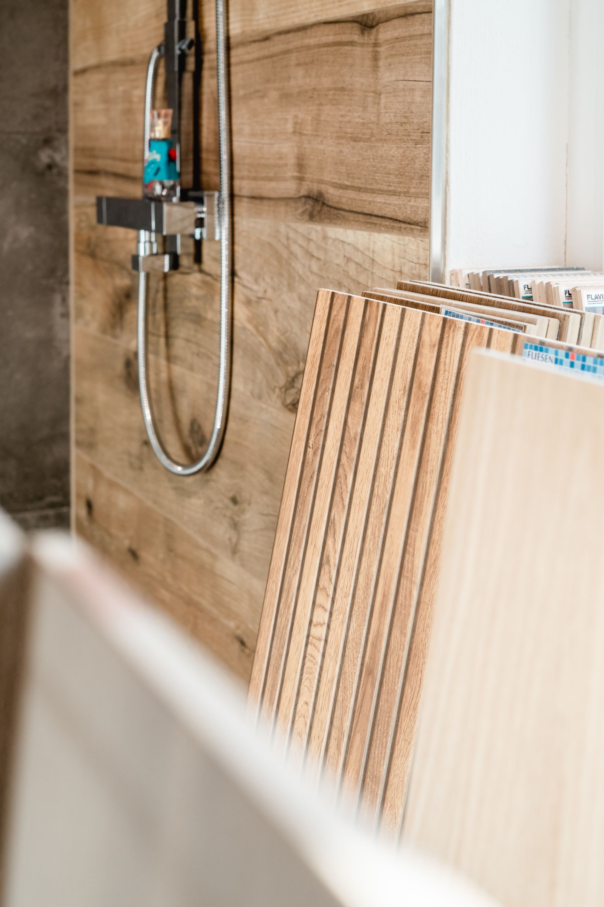 Duschkopf mit Wandverkleidung in Holzoptik und gestapelten Fliesen in einem Badezimmer.