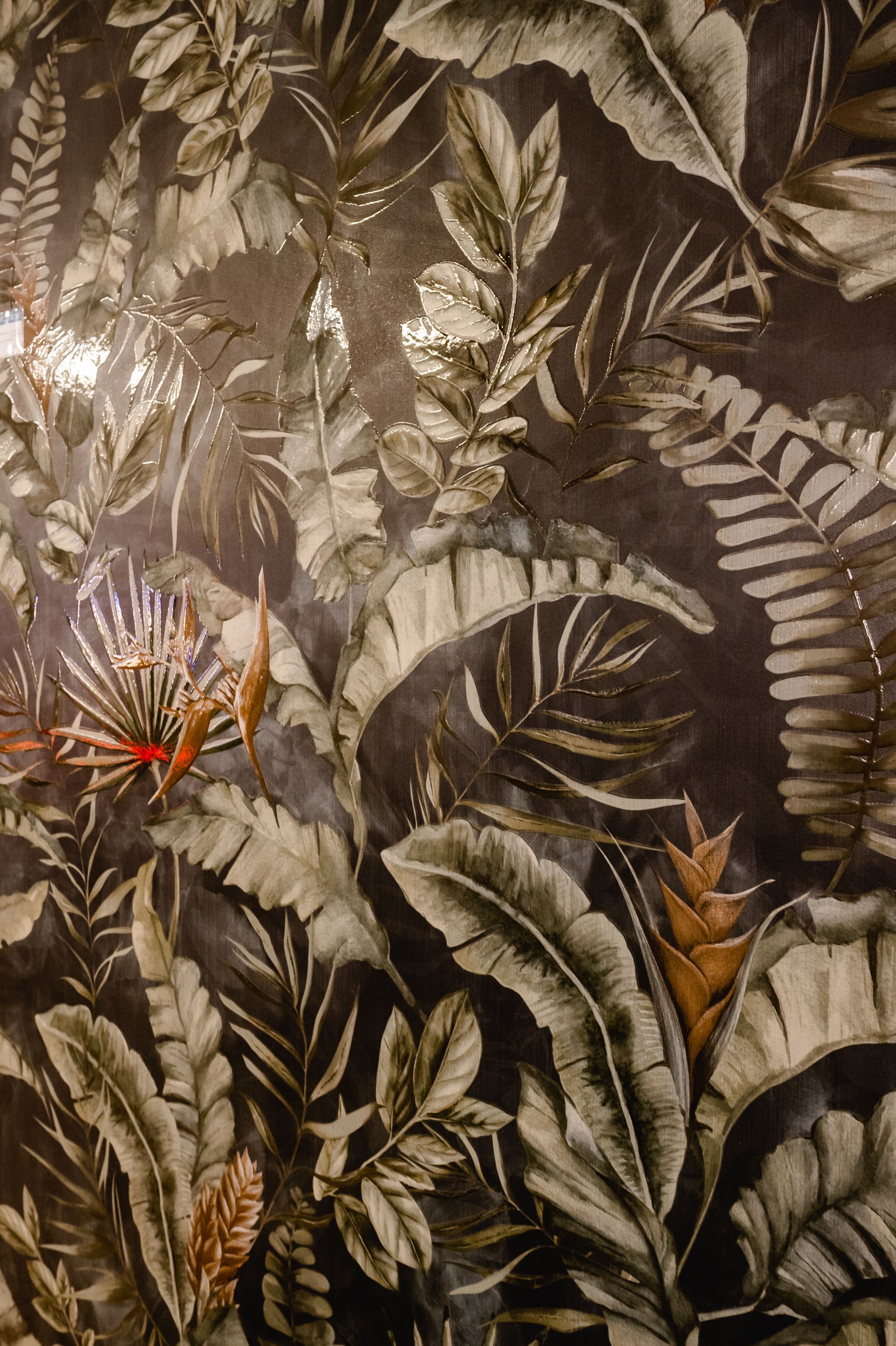 Dunkle Tapete mit tropischem Blumenmuster, mit großen Blättern in Grau-, Gold- und Brauntönen.