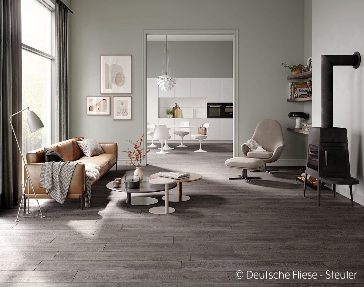 Wohnzimmer mit braunem Ledersofa, Kamin und offener Tür zu einer weißen Küche.