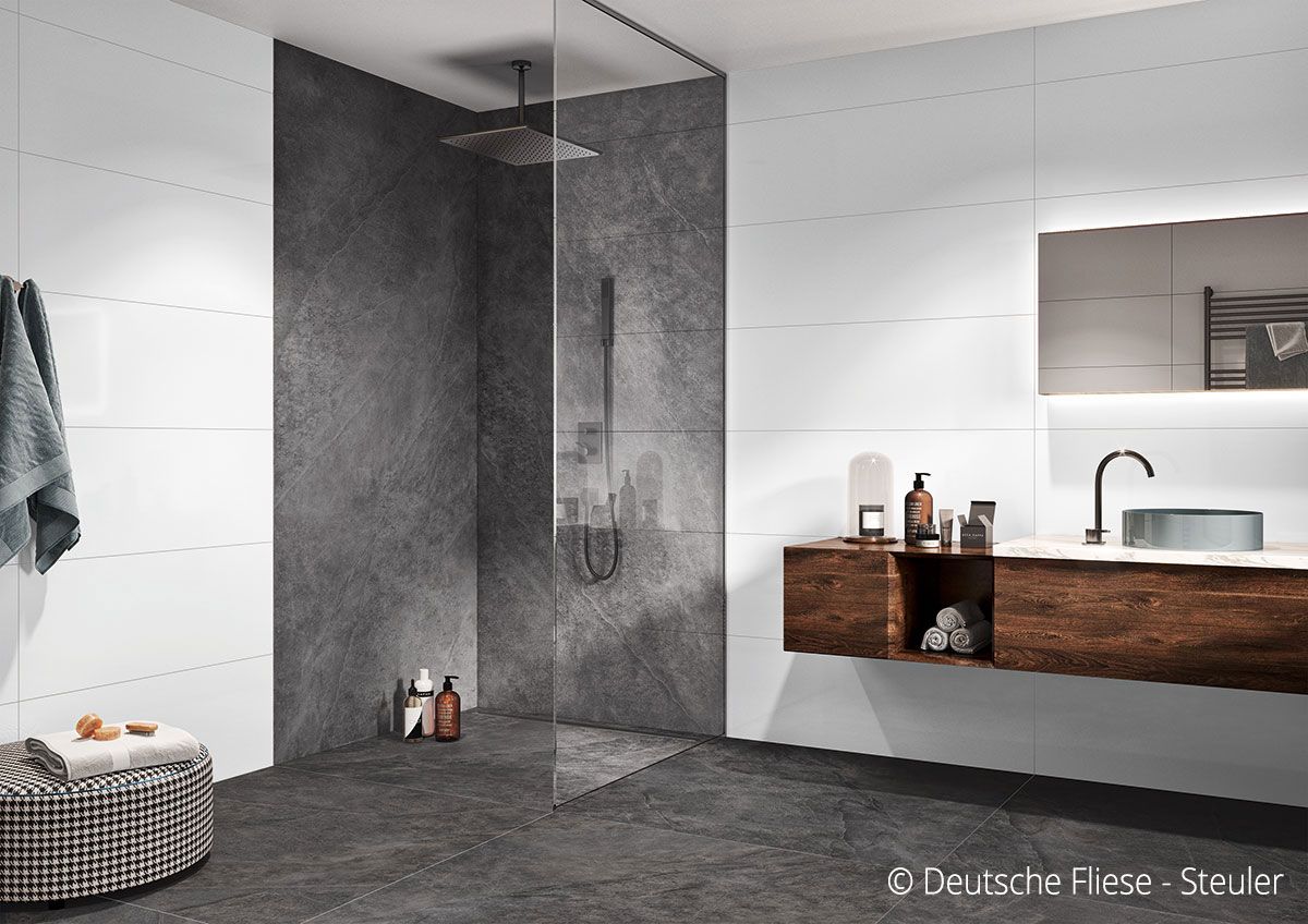 Modernes Badezimmer mit dunkelgrauer Dusche, weißen Wänden, Holzwaschtisch und rundem Hocker.