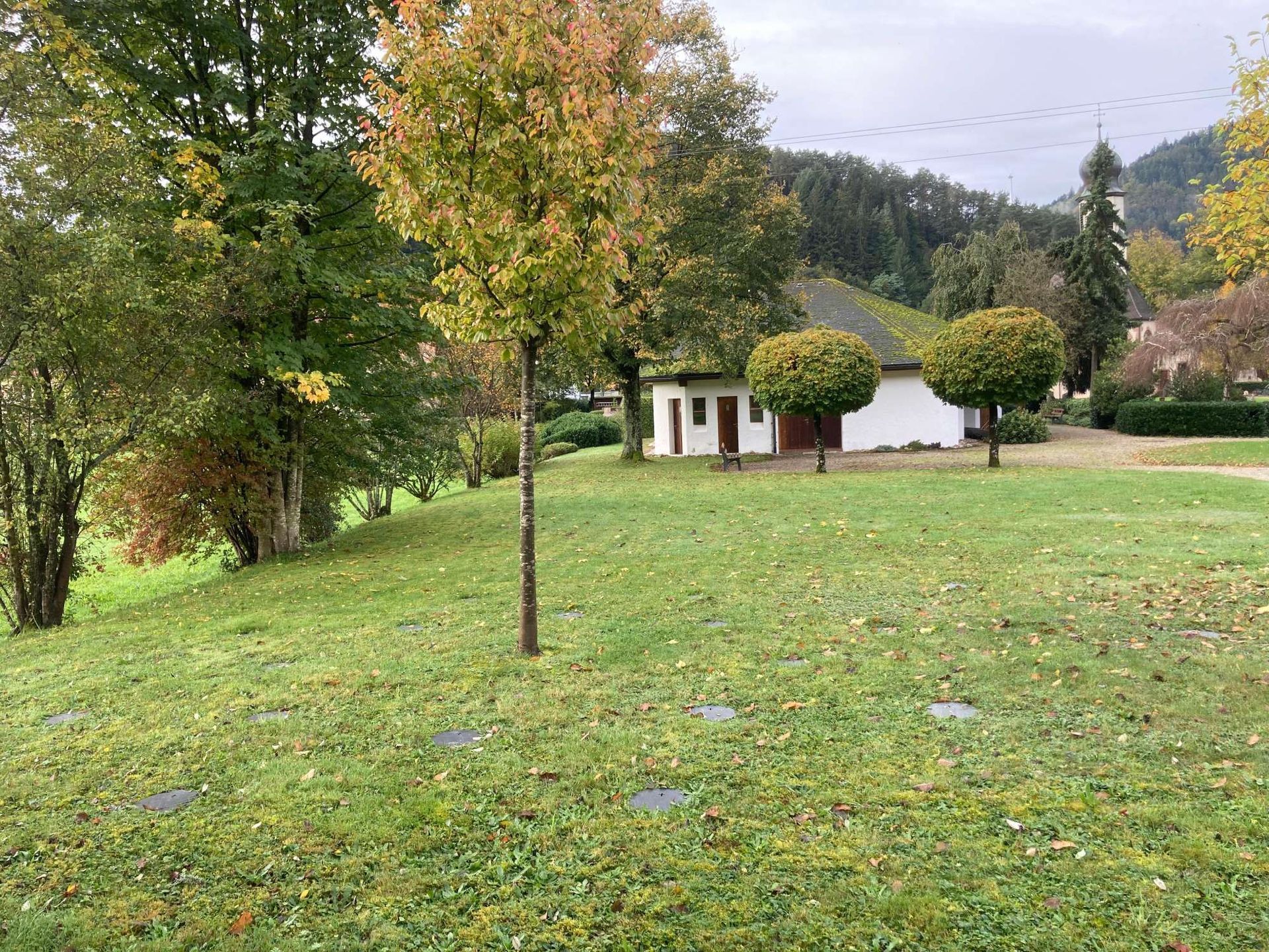 Urne mit Blumenkranz in einer Kirche. Weiße Urne, umgeben von rosa, grünen und roten Blumen.