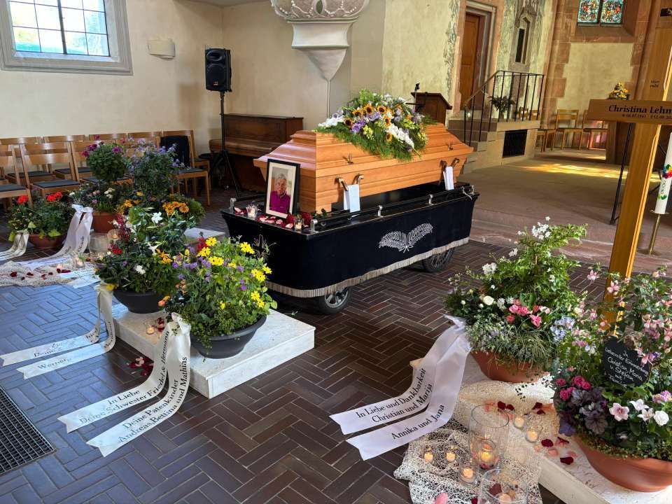 Aufstellung der Trauerfeier: Holzsarg mit Blumengesteck, Kreuz, Kerzen und Blumen.