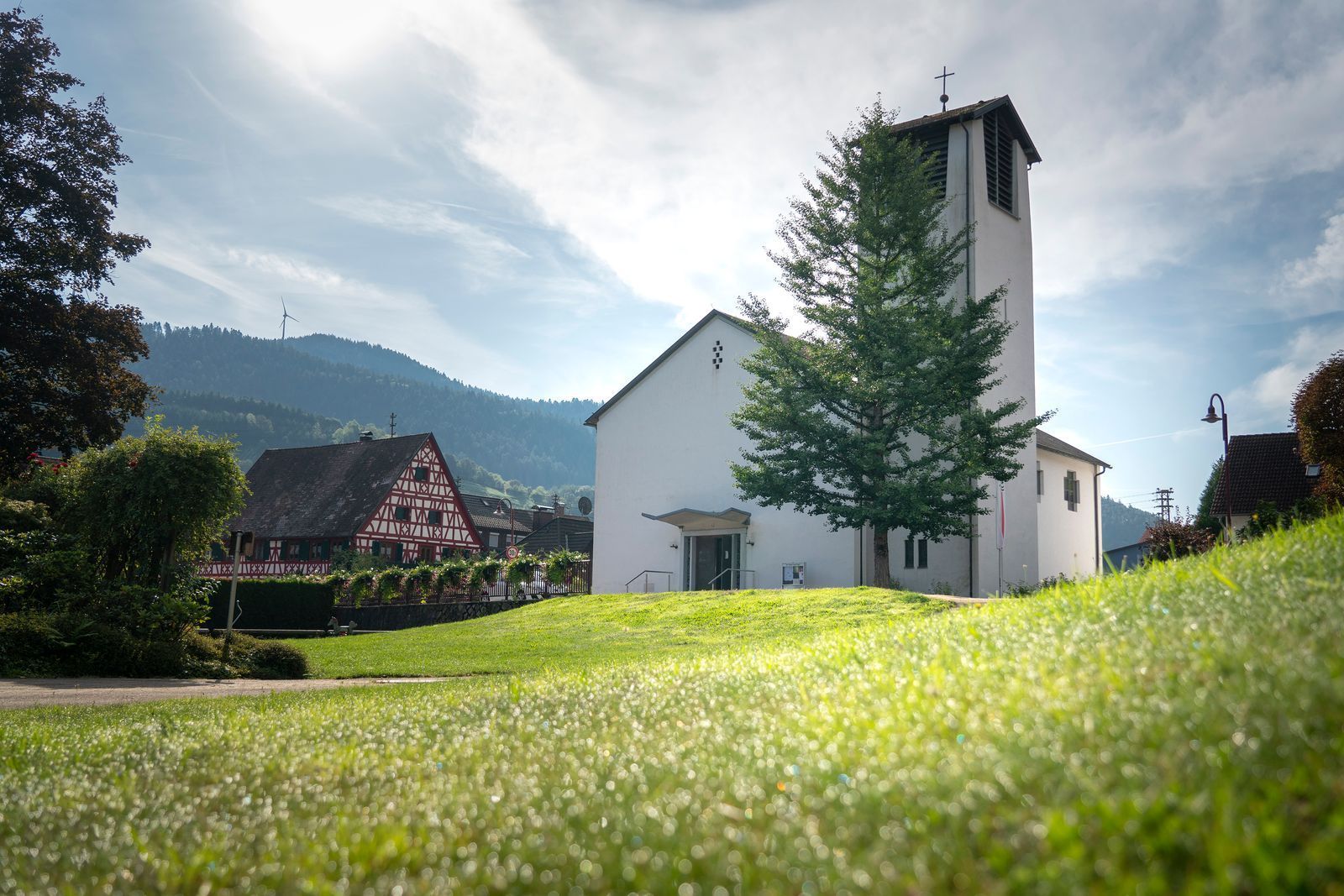 Urne mit weißem Rosenmotiv, umgeben von Blumen, in einer Kirche mit Buntglasfenstern.