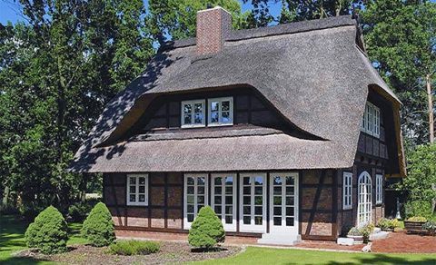 Reetgedecktes Häuschen mit Außenfassade aus Ziegeln und Fachwerk, weißgerahmten Fenstern und grünem Garten.