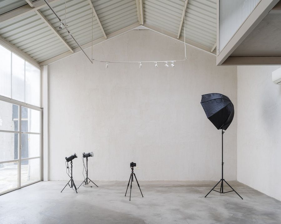 Estudio fotográfico vacío: paredes blancas, tres trípodes con equipo, un softbox grande.