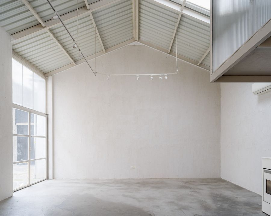 Habitación vacía, de paredes blancas, con suelo de hormigón y techo inclinado. La luz natural entra a raudales.