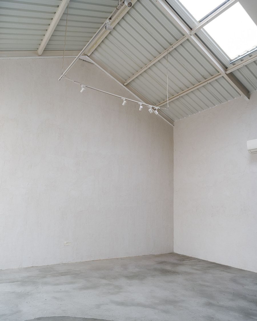 Habitación vacía con paredes blancas, piso de concreto, tragaluz y una pista de luces.