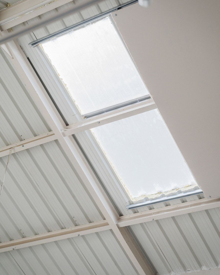 Tragaluz en ángulo en un techo de metal corrugado blanco, con luz que brilla a través de él.