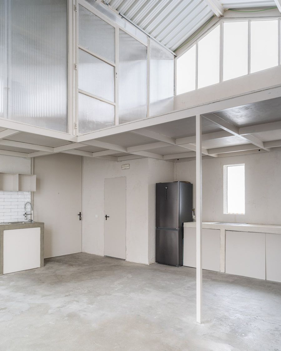 Interior blanco con loft, cocina minimalista, suelo de hormigón, frigorífico negro y paredes translúcidas.