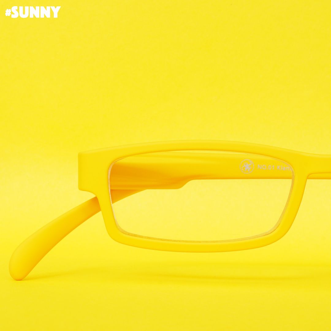 Eine gelbe Lesebrille auf gelbem Hintergrund.