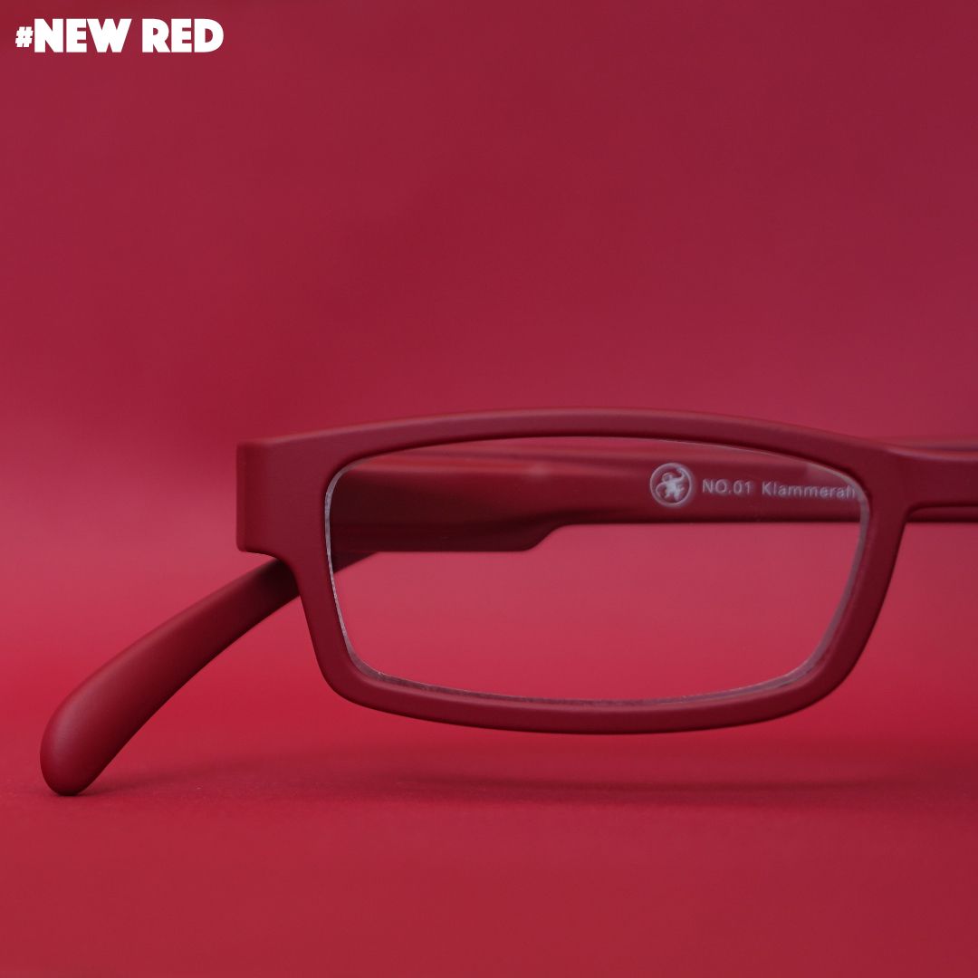 Eine dunkelrote Lesebrille auf rotem Hintergrund.