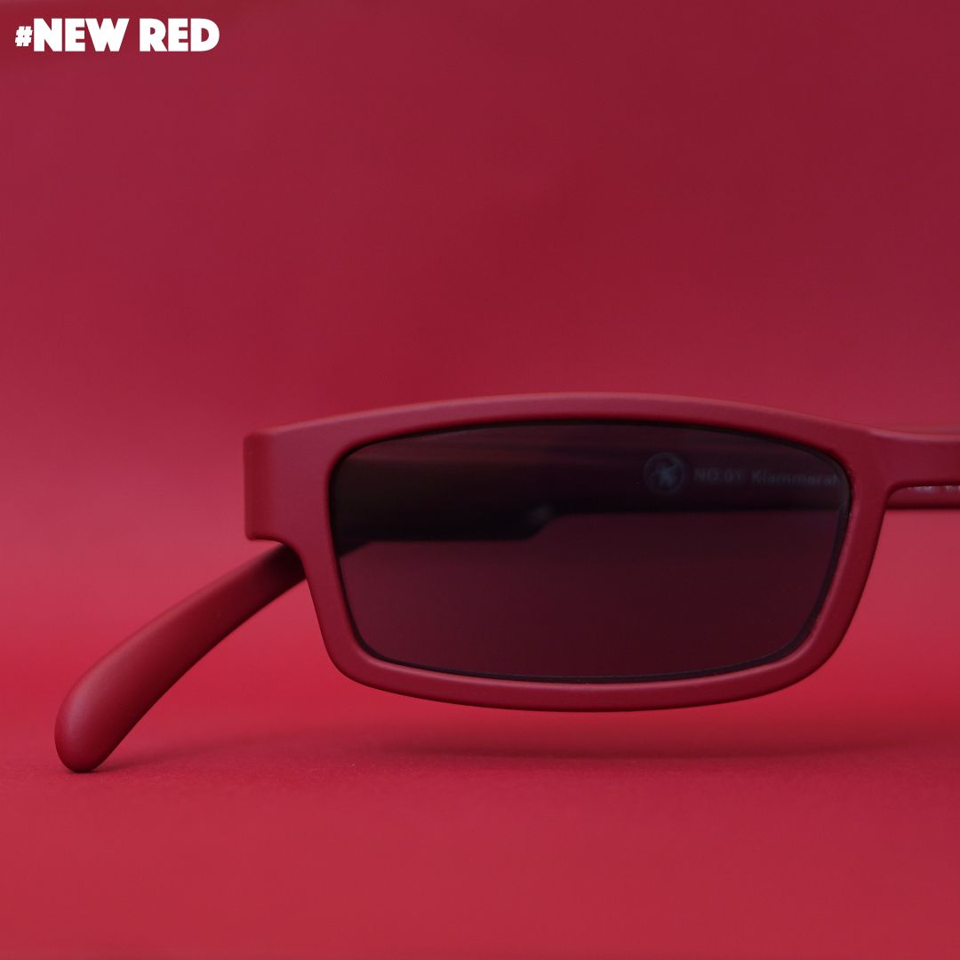 Eine dunkelrote Sonnenlesebrille auf rotem Hintergrund