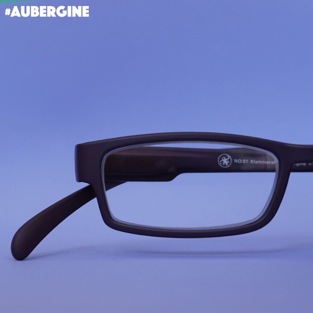 Eine aubergine farbene Lesebrille auf lilanem Hintergrund.