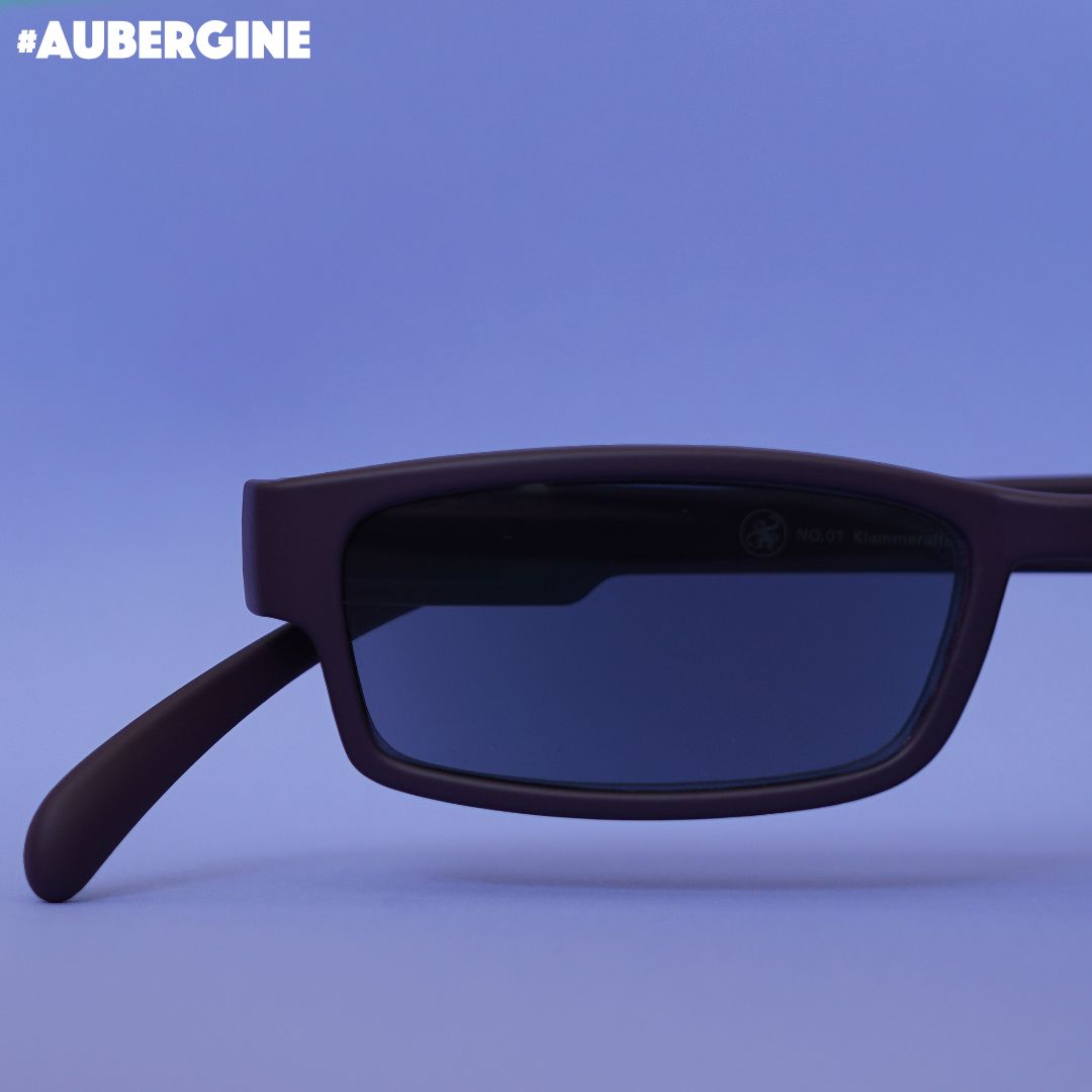 Eine aubergine farbene Sonnenlesebrille auf lilanem Hintergrund