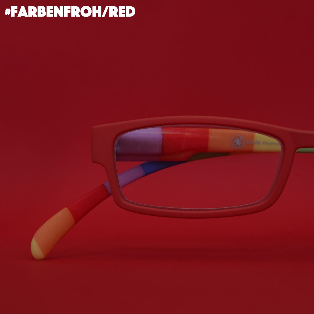 Eine rote Lesebrille mit Bügeln im  gestreiften bunten Look auf rotem Hintergrund.