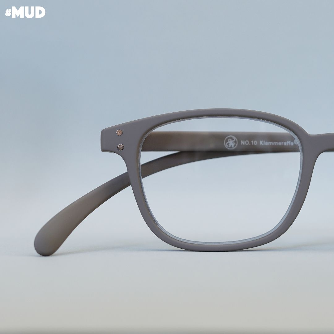 Eine schlamm farbene Brille  auf grauem Untergrund.