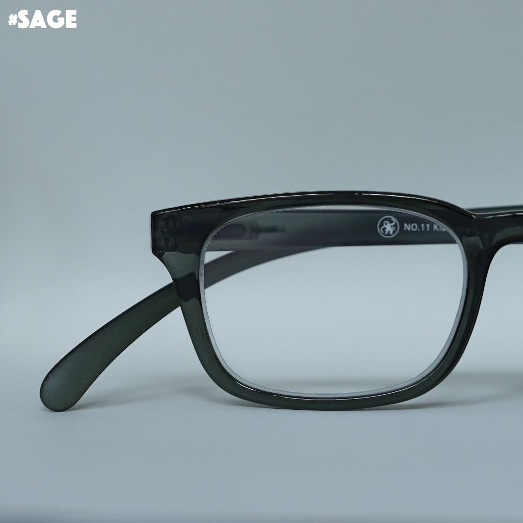 Eine salbei-farbene transparente Lesebrille auf grauem Hintergrund.