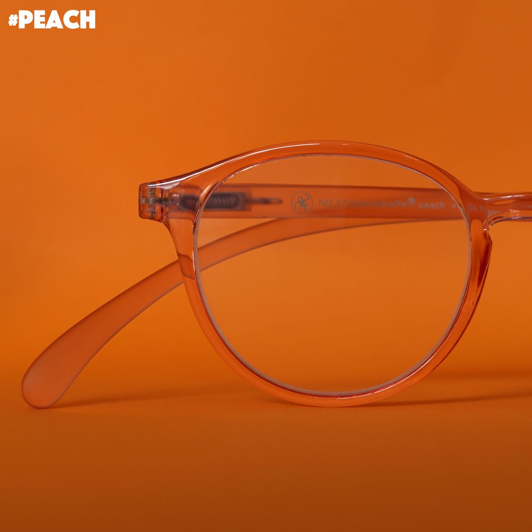 Eine Pfirsich farbene transparente  Brille auf orangenem Hintergrund.