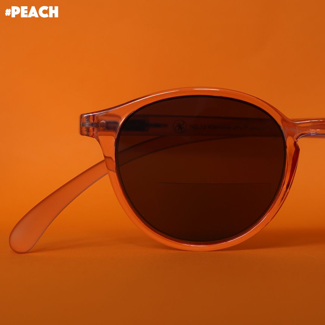 Eine Pfirsich farbene transparente Bifokal-Sonnenbrille auf orangenem Hintergrund.