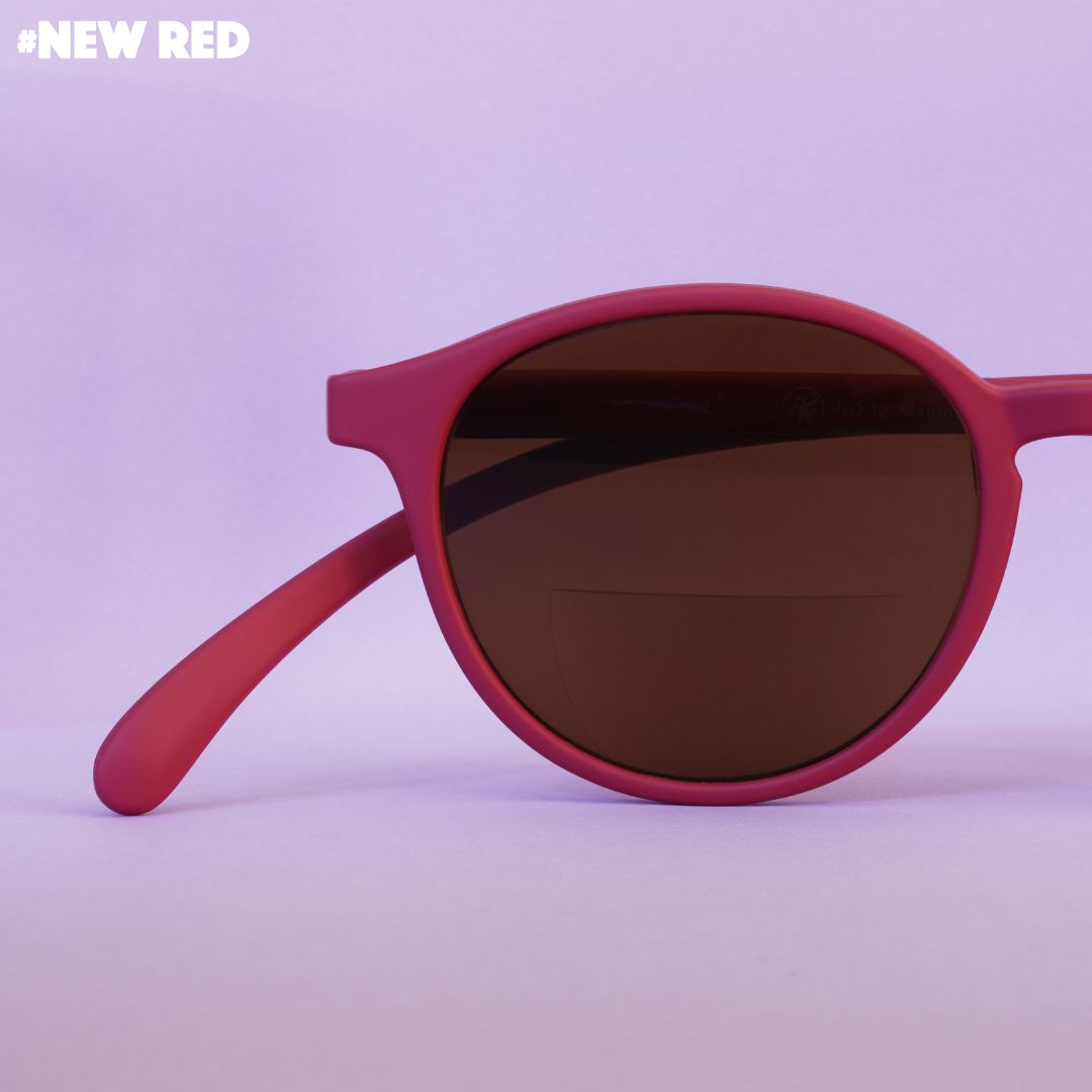 Eine rote Lesebrille auf rosa farbenem Hintergrund.