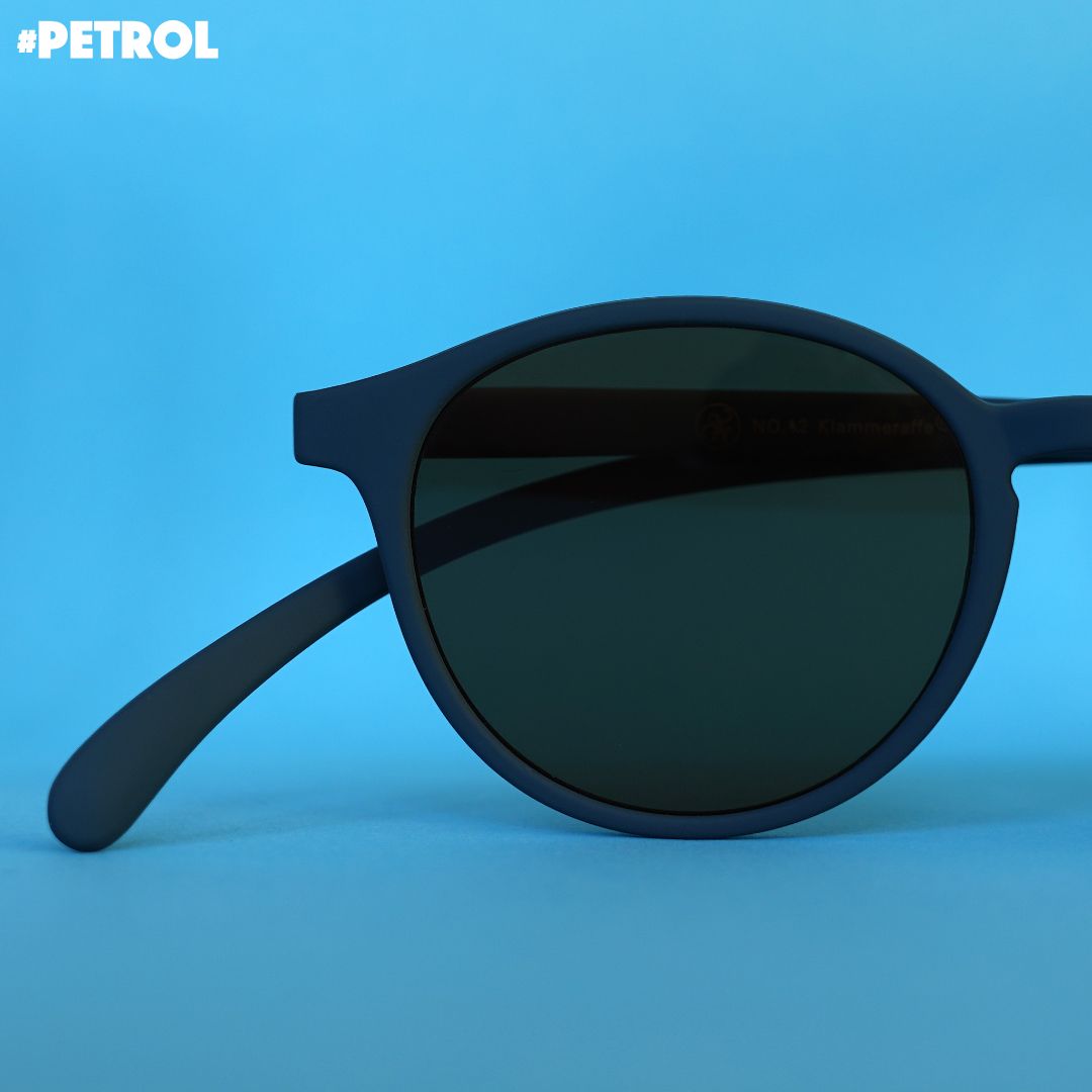 Eine petrol farbene Sonnenbrille auf blauem Hintergrund.