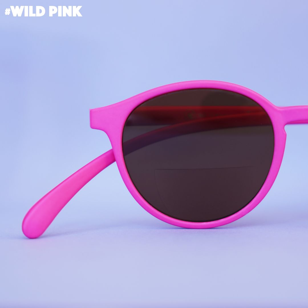 Eine pink farbene Lesebrille auf flieder farbenem Hintergrund.