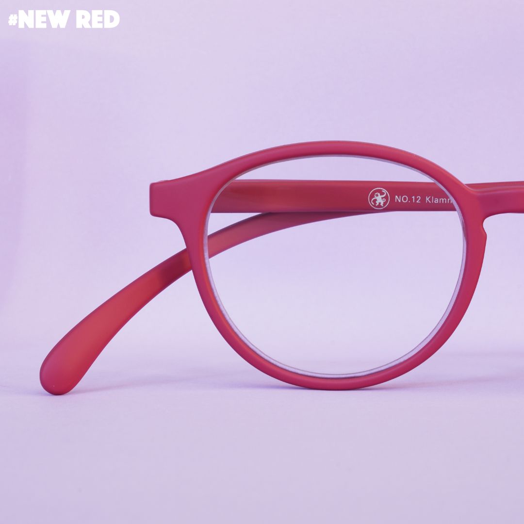 Eine rote Lesebrille auf rosa farbenem Hintergrund.