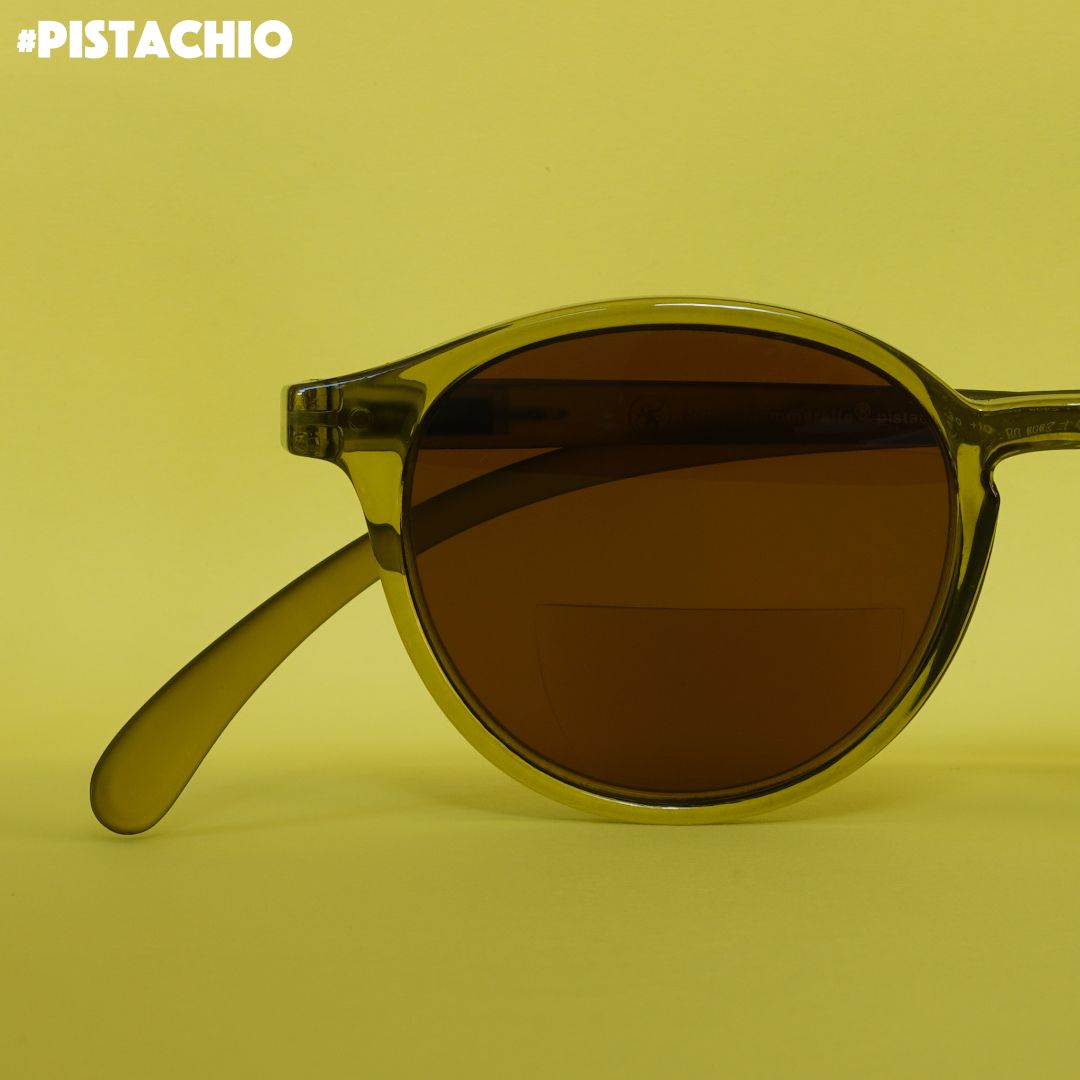 Eine Pistazien farbene transparente Bifokal-Sonnenbrille auf grünem Hintergrund.