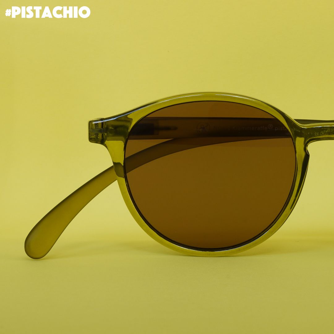 Eine Pistazien farbene transparente Sonnenbrille auf grünem Hintergrund.