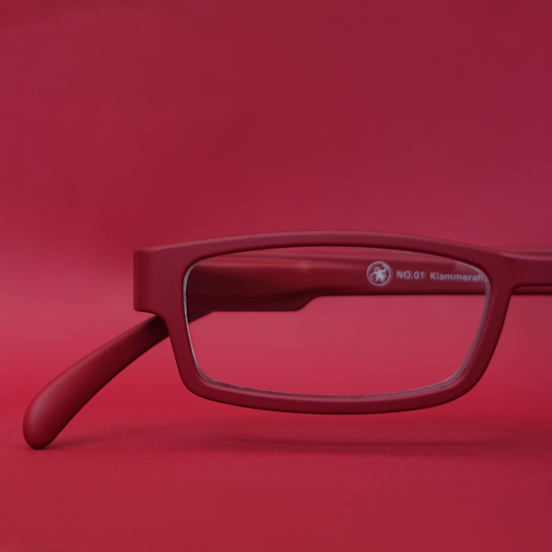 Rote Brille mit einem verlängerten Bügel vor einem passenden roten Hintergrund.