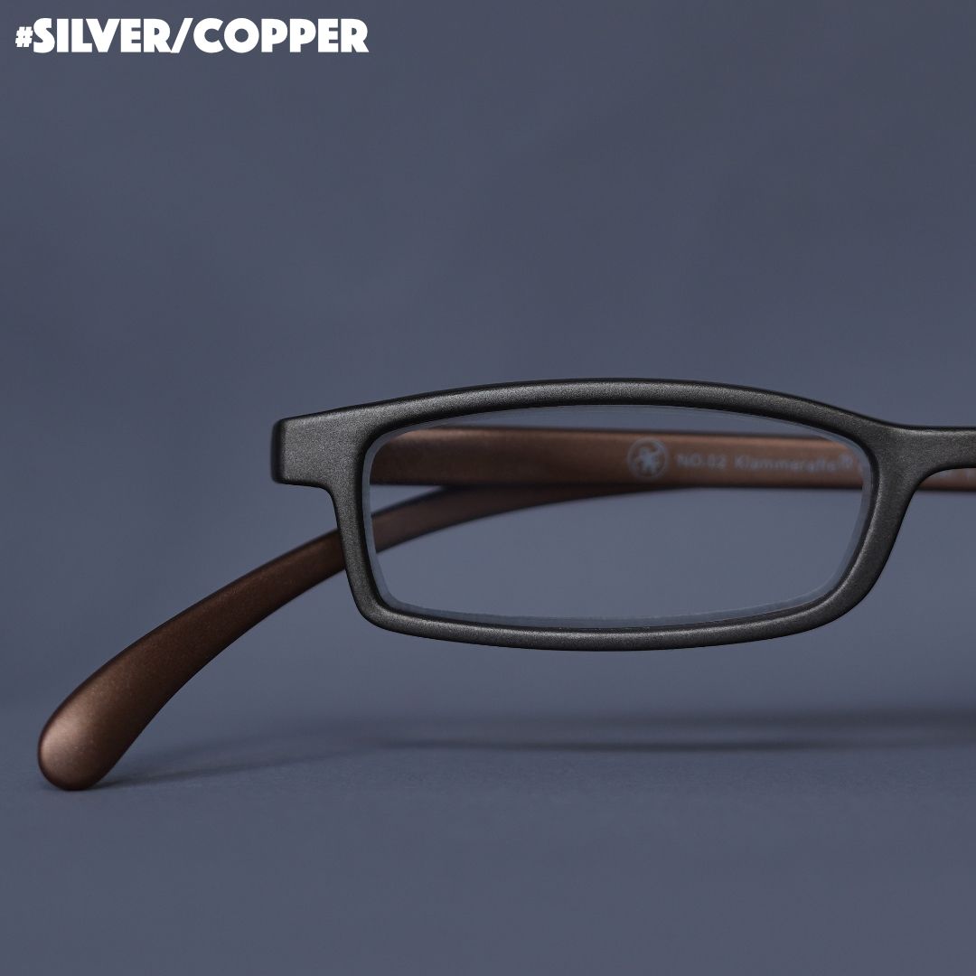 Eine silver-goldene Lesebrille auf grauem Hintergrund.