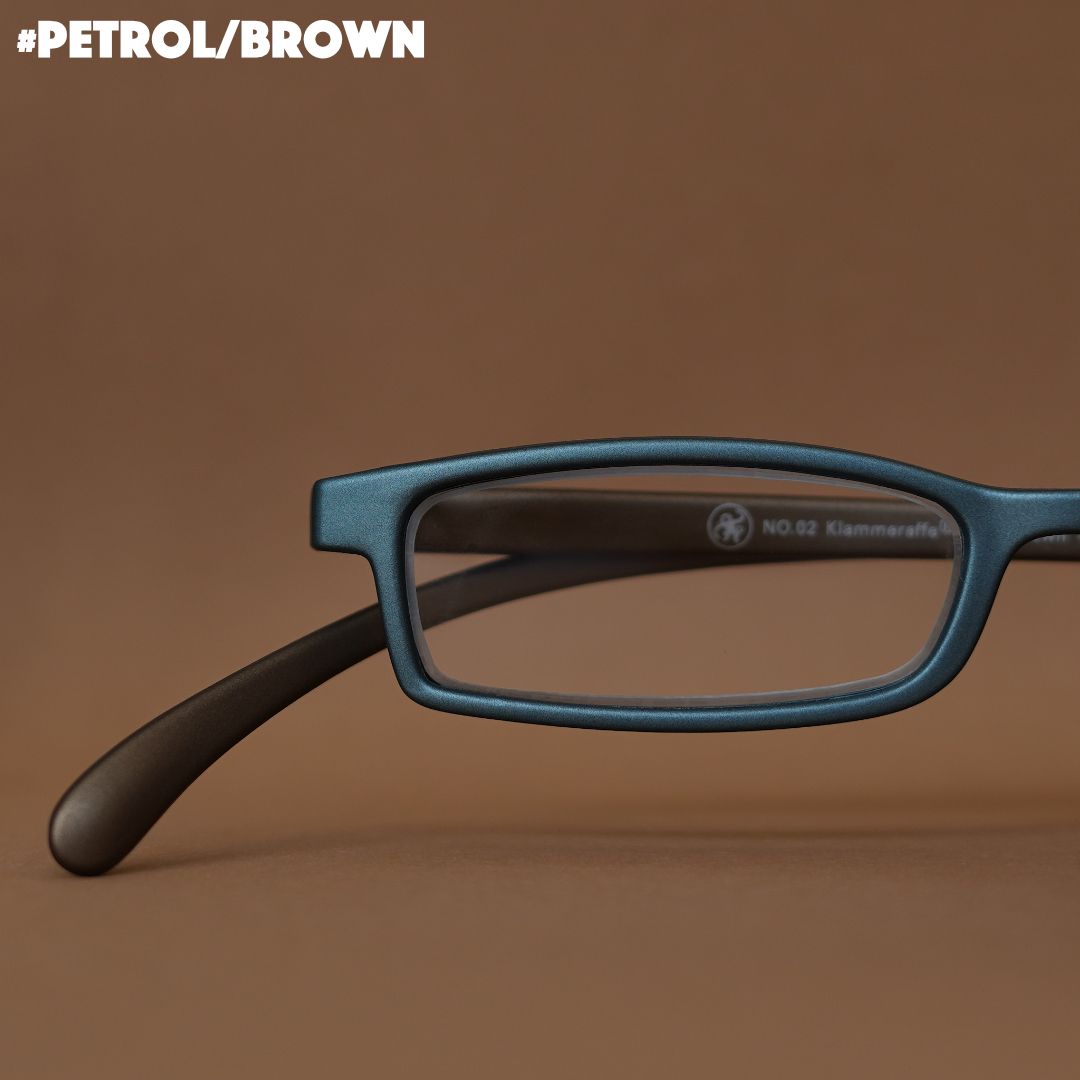 Eine petrol-braune Lesebrille auf braunem Hintergrund.