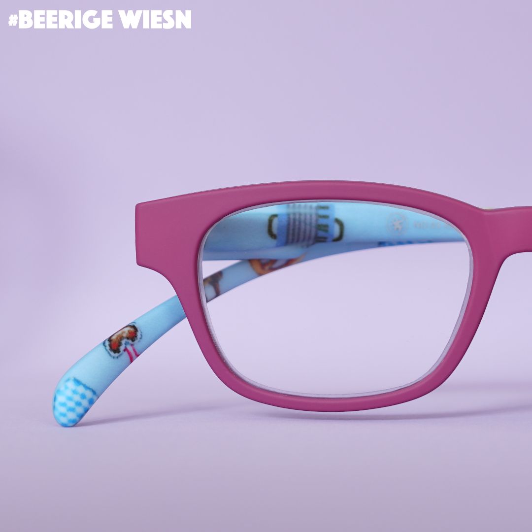 Eine rote Lesebrille mit blauen Wiesn Look Bügeln auf fliederfarbenem Hintergrund.