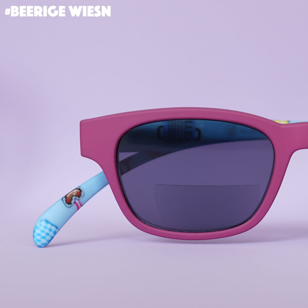 Eine rote Bifo-Sonnenbrille mit blauen Bügeln im Wiesn Look auf fliederfarbenem Hintergrund.