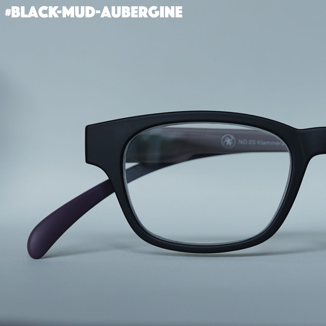 Eine schwarz-aubergine farbene Lesebrille auf grauem Hintergrund.
