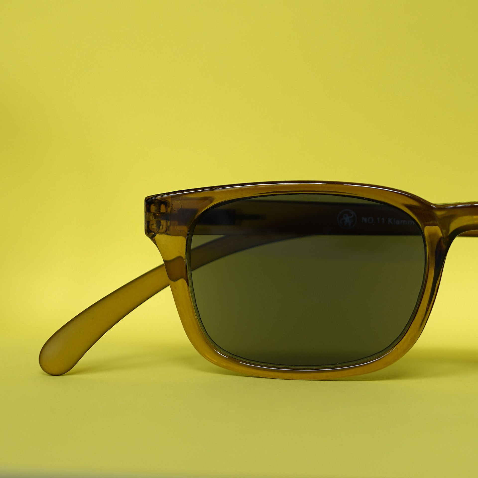 Sonnenbrille mit braunem Rahmen und dunklen Gläsern auf gelbem Hintergrund.