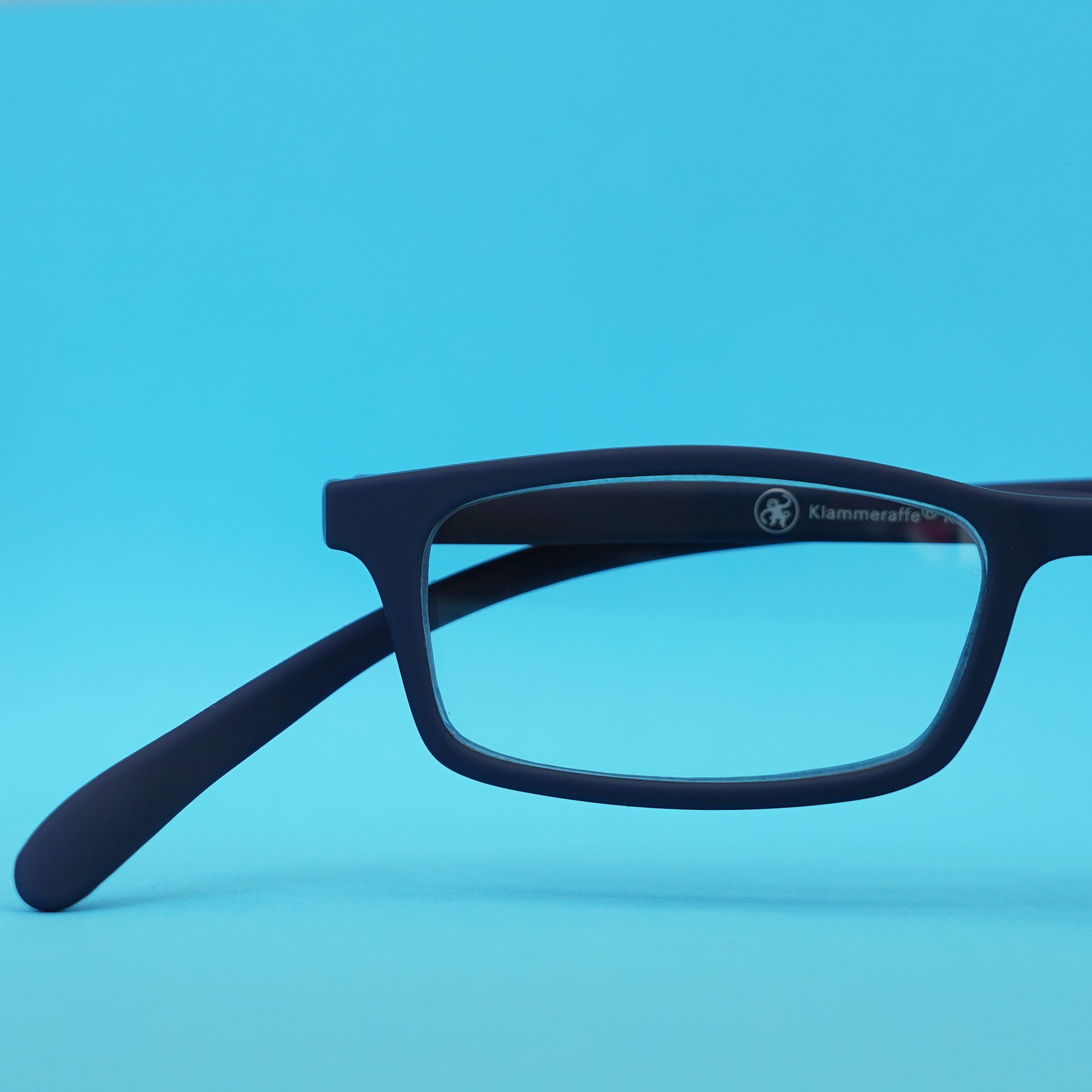 Marineblaue rechteckige Brille auf hellblauem Hintergrund. Ein Bügel ist verlängert.