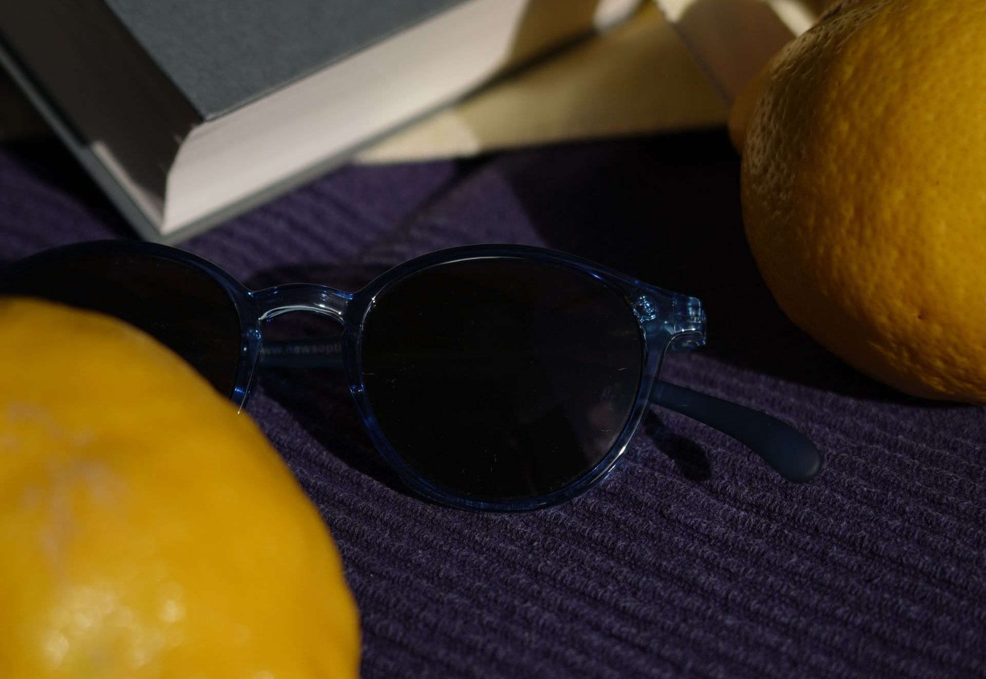 Auf einem Tisch liegt eine Sonnenbrille neben Zitronen und einem Buch.