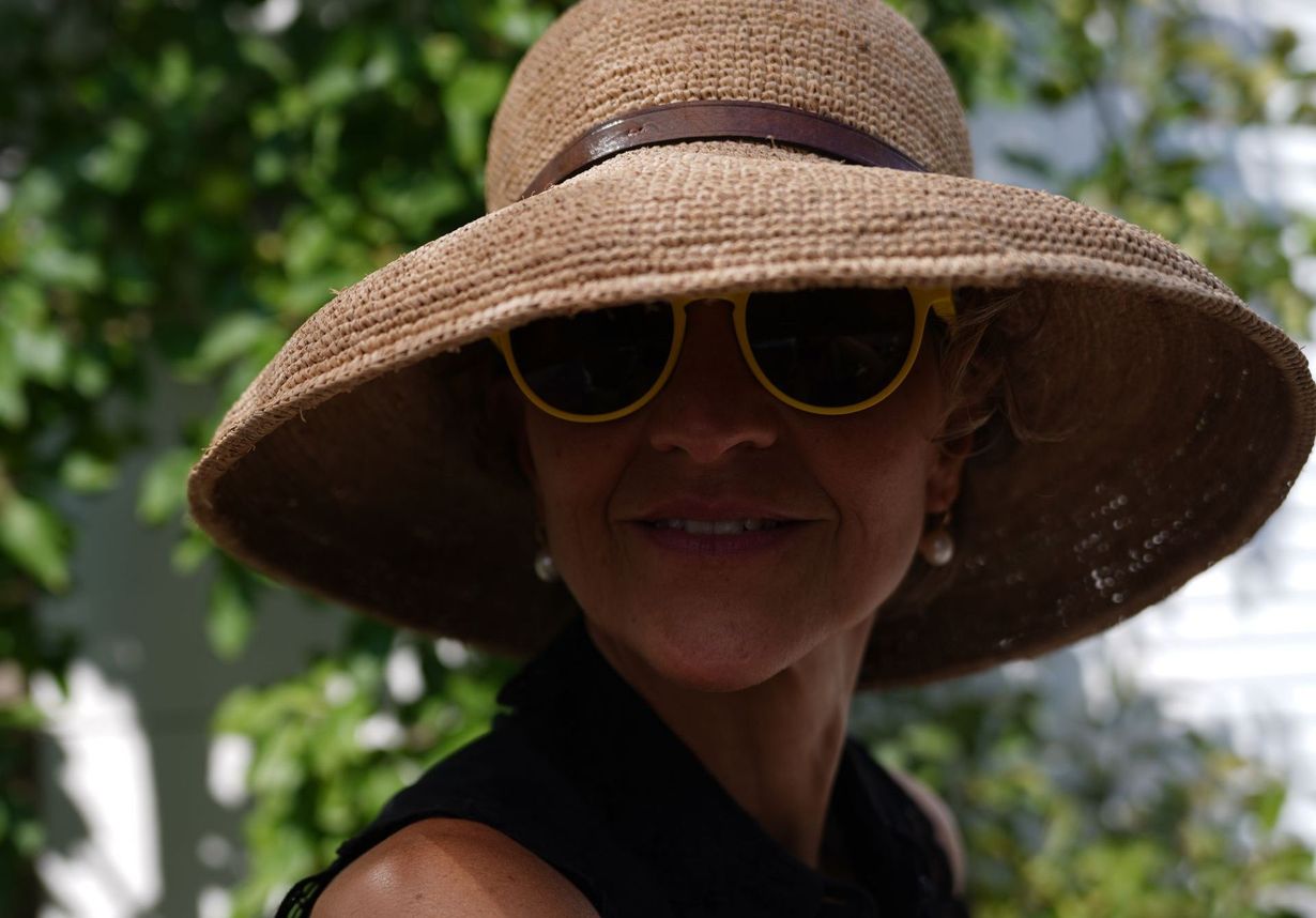 Eine Frau mit Hut und Sonnenbrille lächelt.