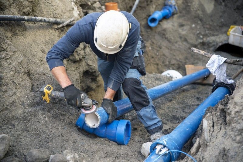 Arbeiter bei einer Rohrsanierung in offener Bauweise beim Reparieren eines Abwasserrohrs in einer Baugrube