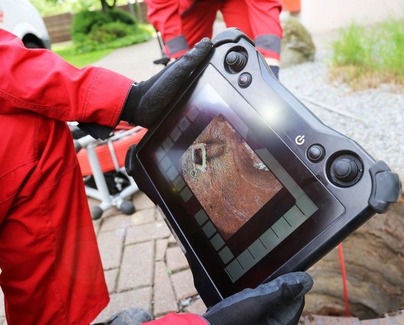 Rohrsanierung in Kamen: Mitarbeiter von KN Kanaltechnik hält ein Monitorgerät mit Livebild der Kanalinspektion per TV-Kamera am geöffneten Schacht.