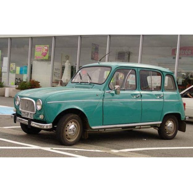 Un coche verde está estacionado en un estacionamiento frente a un edificio.