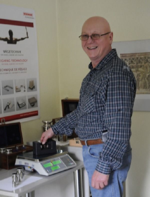 Mann steht vor einer Industriewaage und lacht